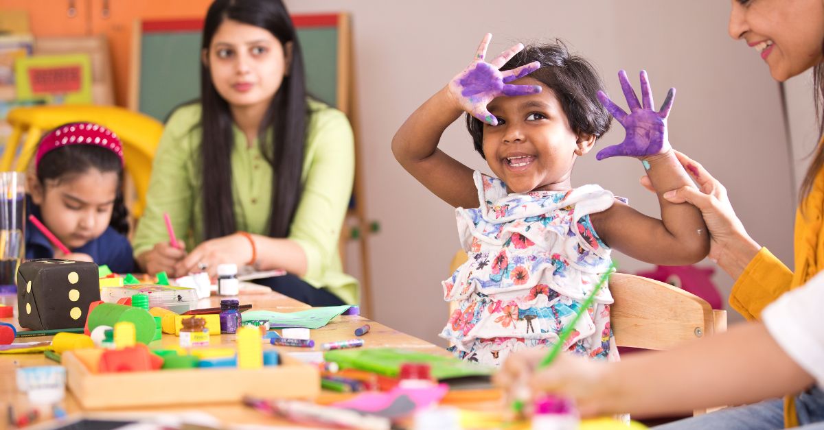 Preschooler smiling at the camera while finger painting at school