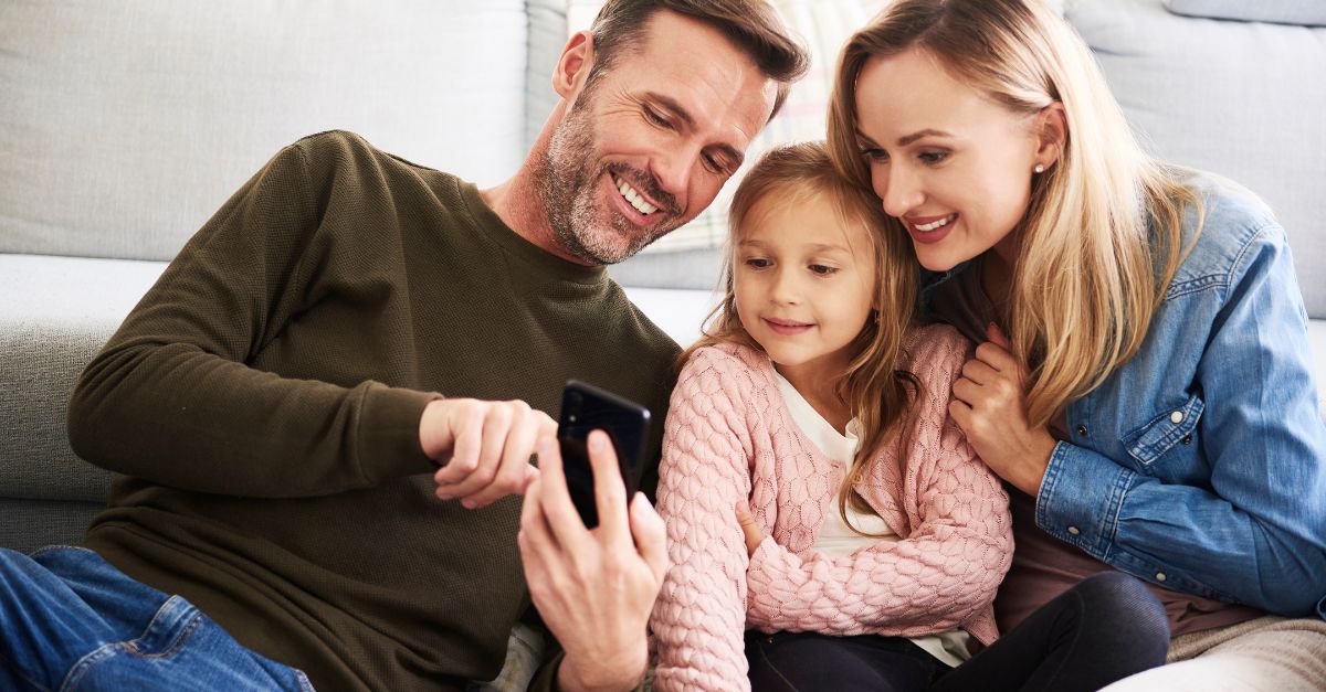 Parents and their daughter looking at updates from their childcare on their mobile phone