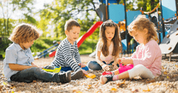 Four preschool aged children playing with sand and shovels at an outdoor playground