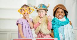 Group of three preschool girls smiling at the camera as they play dress up