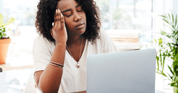 A home childcare provider sitting at their computer with their eyes closed and feeling overwhelmed. 