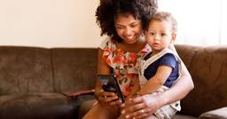 Parent holding infant and looking at phone as she receives online communication from her childcare center