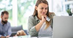 Mom sitting at laptop smiling, holding credit card and paying childcare tuition fees online