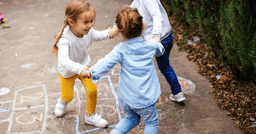 Three preschool aged children holding hands in a circle and smiling as they spin around