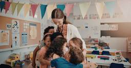 Preschool children hugging their teacher who may be experiencing burnout despite enjoying her job